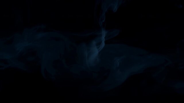 Blue smoke rising in slender curling plume against deep black background with soft translucent wisps spreading outward and fading into shadowy space, with smoke, vapor, mist, blue detail