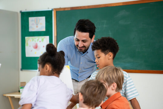 Caucasian male teacher teaching art lesson to children in classroom. 