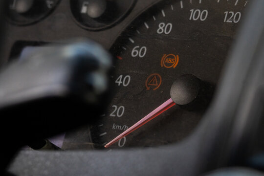 Instrument cluster with speed scale in kilometers shows ABS and hazard indicators illuminated while the steering column edge frames the view creating a close look at dashboard status