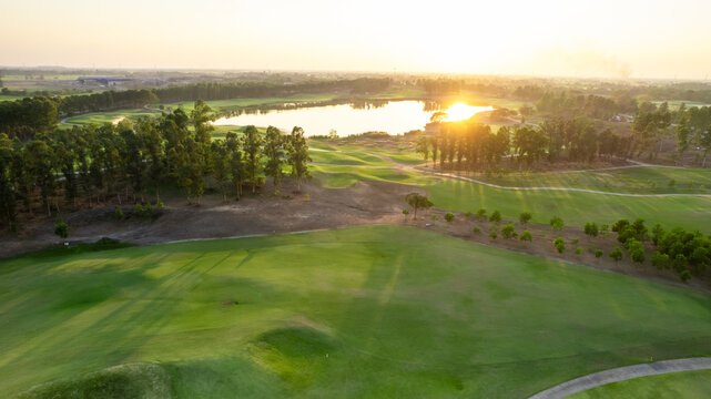 Aerial drone view flying over empty golf course near lake with lush greenery.