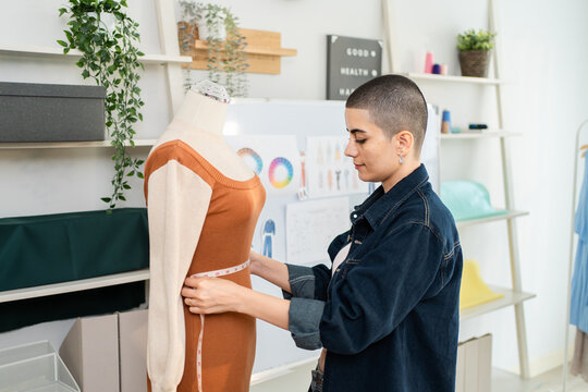Caucasian woman with shaved head hairstyle working as fashion designer in studio. 