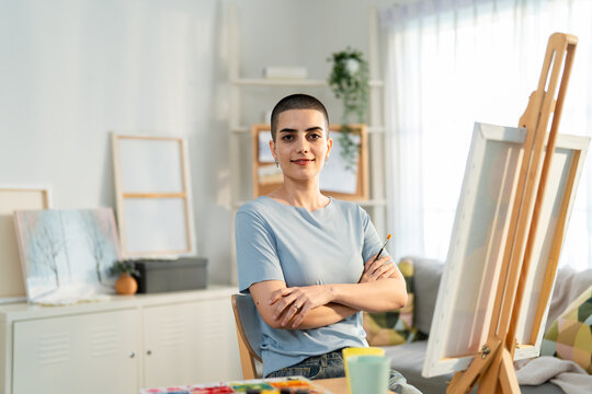 Portrait of female artist painting artwork on canvas frame at home studio. 