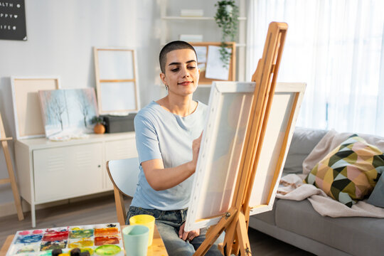 Caucasian female artist painting artwork on canvas frame at home studio.