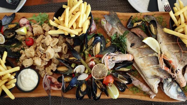 Seafood feast with grilled whole fish mussels shrimp squid and french fries fills a wooden platter creating a generous restaurant meal for sharing during summer vacations