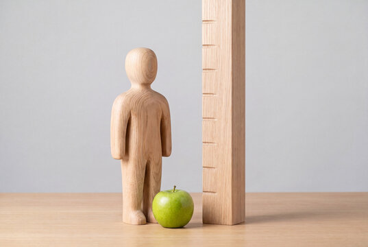 Height measurement and healthy growth concept, wooden figure beside a notched measuring post and a green apple