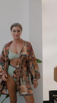 Elegant woman wearing luxury kimono robe over  swimsuit in modern tropical villa.