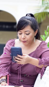 Woman Sitting on Park Bench Checking Smartphone While Drinking Orange Juice