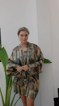 Elegant woman wearing luxury kimono robe in modern tropical home.
