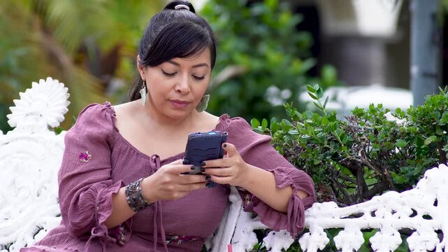 Woman Sitting on Park Bench Checking Smartphone in Peaceful Outdoor Setting