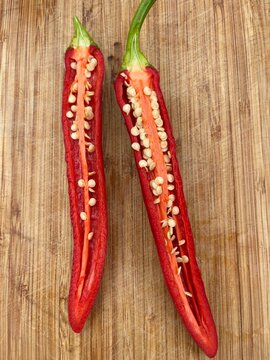 Top view of red chili pepper sliced lengthwise revealing white seeds on wooden cutting board background