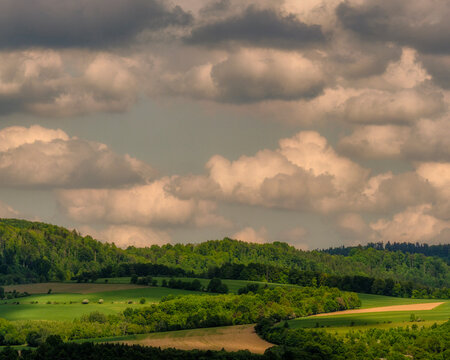 Gentle white clouds floating over lush green rolling hills and countryside forests