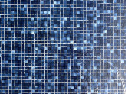 Clear swimming pool water under sunlight. Deep blue mosaic tiles on pool floor.