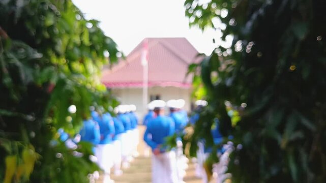 Blurred View of Indonesian Students in Blue Uniforms for School Ceremony Through Green Leaves