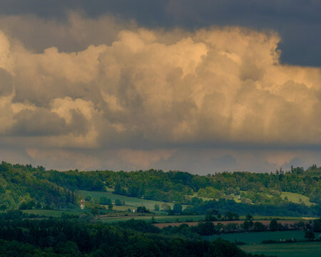 Dense dramatic cloud formations hanging low over lush green rolling hills and forests