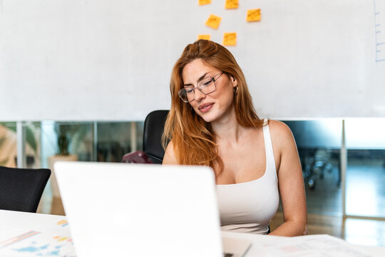 Business woman working on laptop at office desk. Corporate management and strategy, Smiling female manager wearing glasses looking at computer screen in modern workplace. Professional employee.