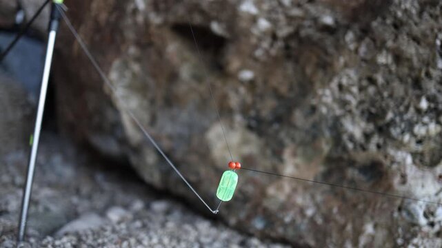 Fishing float hangs motionless on a fishing line beside a rocky shore showing a quiet waiting moment before a bite during a calm recreational angling session outdoors now