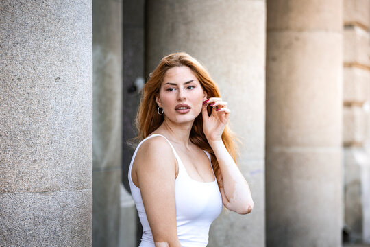 Portrait of a young woman on city street. Urban fashion and lifestyle, Attractive female model touching earring near stone pillar and classic architecture building exterior.