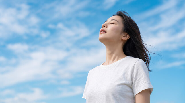 青空の下で両手を広げて深く息を吸い深呼吸する若い女性のリフレッシュシーン