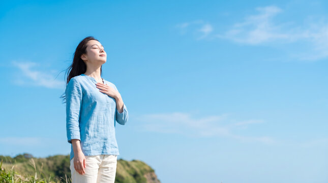 青空の下で両手を広げて深く息を吸い深呼吸する若い女性のリフレッシュシーン