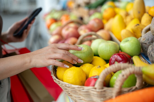 Close up of woman's hands selecting or buying fruit while holding phone and shopping in fresh market