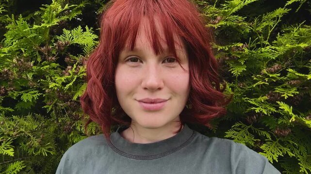 A beautiful young woman with red hair and a bob haircut looks at the camera against a green wall.