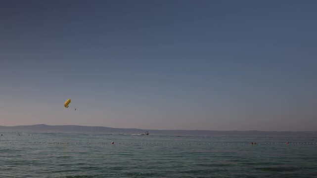 Parasailing above calm seas as a speedboat pulls a yellow parachute along the coastline creating a scenic summer adventure while swimmers relax in clear blue water nearby