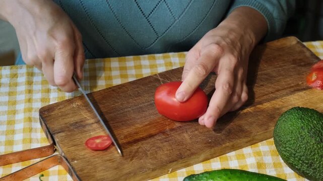 Food prep. Female hands slicing tomato for salad on wooden board. 
