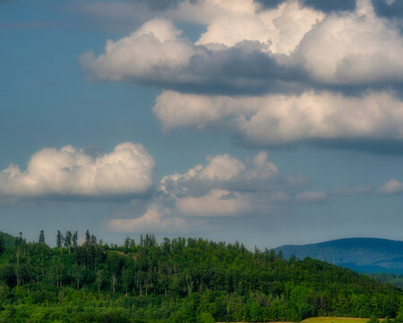 Light fluffy clouds scattered across a bright blue summer sky above a distant green horizon line, peaceful natural landscape