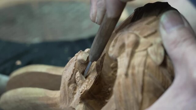 Detailed hand carving of an ornamental relief figure on a wooden craft object using a narrow gouge