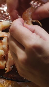 Vertical video. Food prep. Female hands peeling boiled tiger prawns. Eating seafood.