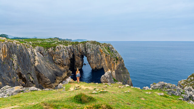 woman tourist looking at natural rock arch cliff and atlantic ocean in asturias spain. Debo del diablo in Ribadesella