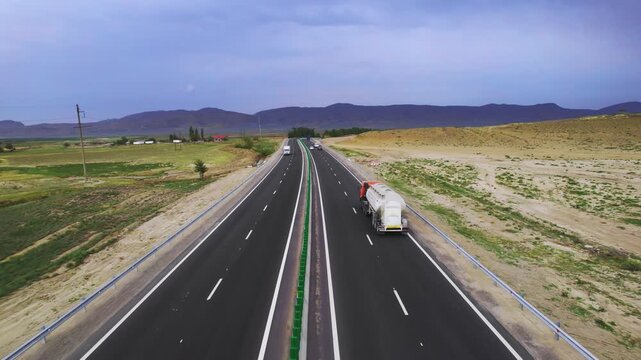 Cinematic drone view presents tanker truck and cars beneath gathering dark clouds as the drone tracks forward above the central divider highlighting infrastructure depth and North Caucasus
