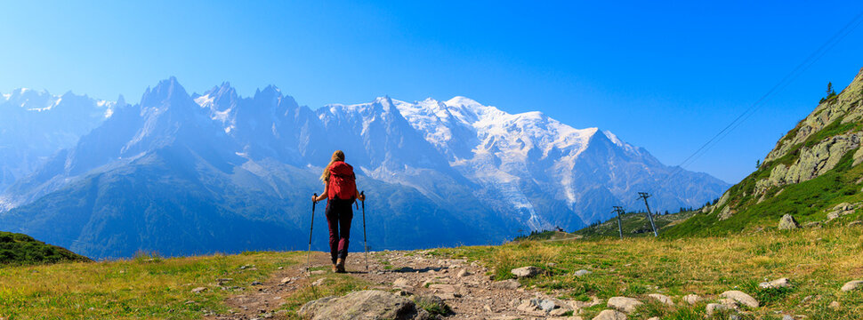 female hiker walking with red backpack and poles toward snowy mont blanc massif in chamonix france