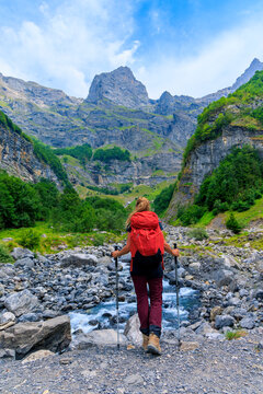 female hiker with red backpack looking at Alps mountain peak and river in valley, Circus of sixt fer a cheval, Chamonix