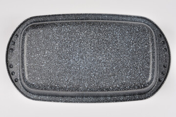 A top down shot shows the bottom of an upside down rectangular speckled roasting pan resting on a plain grey surface. © nahhan