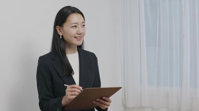Young Japanese businesswoman taking notes on binder smiling in front of white wall