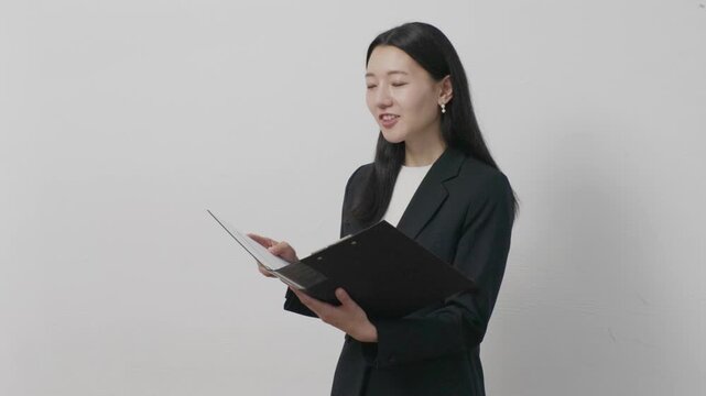 Young Japanese businesswoman looking at file smiling in front of white wall
