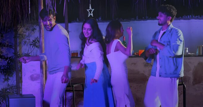 Indian young adult gen z male female couple group hold glass drink juice dancing on music sing song have fun joy. Happy girl boy man woman pair standing at bar table spend time enjoy night party place