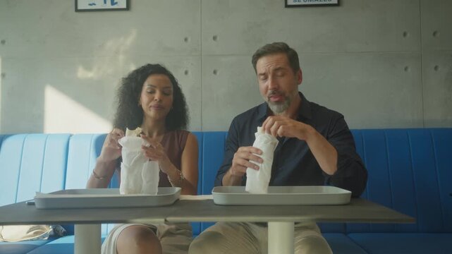 Smiling diverse couple eating tortillas together in casual fast food restaurant