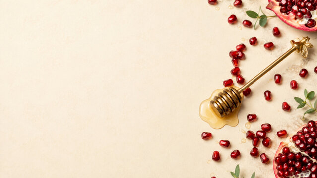 Scattered pomegranate seeds and honey spoon on cream background