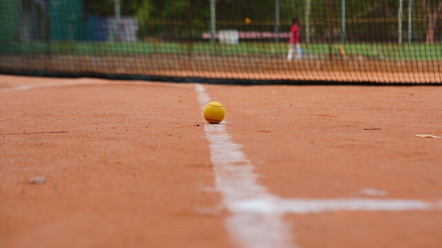 Yellow Tennis Ball Resting on White Line of Clay Court