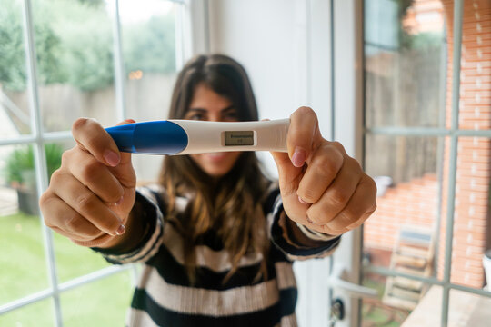 A white woman holds a digital pregnancy test inside near a window