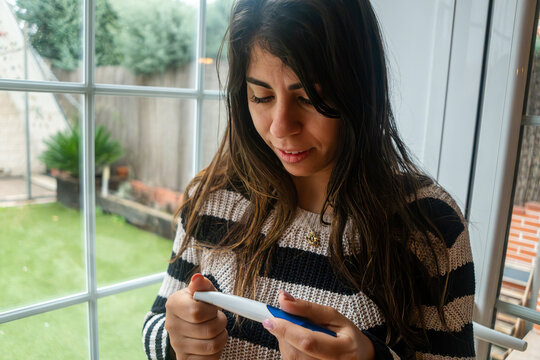 White Woman reads pregnancy test result in her home by a window