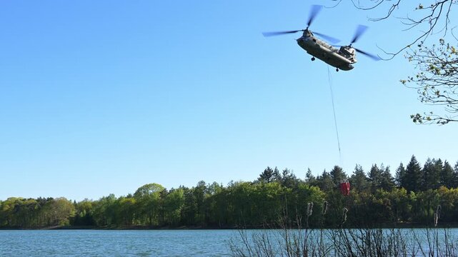 Chinook Transport helicopter of The Royal Netherlands Air and Space Force carrying a water bucket or bambi bucket for extinguishing wildfires in nature loads water into the bucket to put out a wWildfi