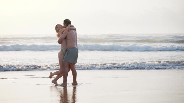 Young couple enjoying a playful moment while spinning together on the beach at sunset. Freedom, happiness, outdoor lifestyle, travel and unforgettable summer memories concept.