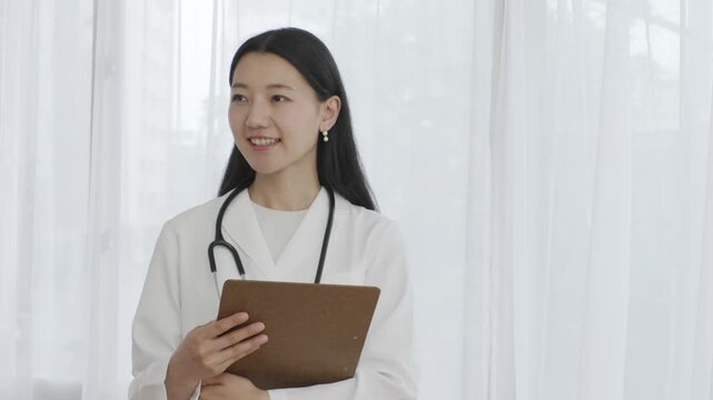 Young Japanese female doctor holding binder smiling by window