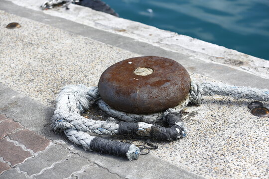 Rusty Mooring Bollard Secures Ropes Beside Harbor Water.
