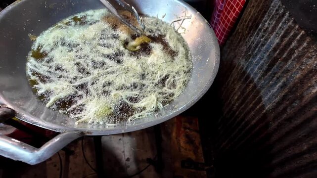 Close-up of a street food vendor pouring thin batter into boiling oil in a large wok to prepare a traditional Thai fried dessert at a night market. Authentic Asian street food cooking with bubbling oi
