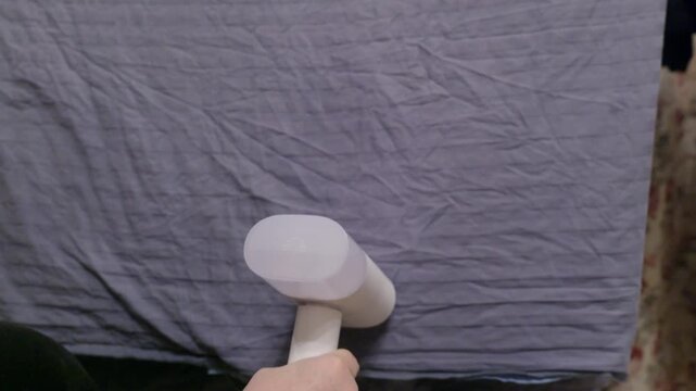 Person demonstrates portable steamer device on crumpled gray textile surface, includes high quality original audio capturing device operation sound.