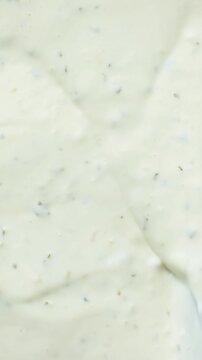 Culinary vertical background with a spatula sliding through thick white garlic dressing.